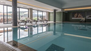 An indoor swimming pool with lounge chairs and a view of a bridge. - Vila Gale Collection Douro Hotel (Lamego)