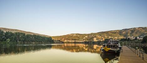 A calm river with a wooden dock and a boat named 'Caminhos do Douro'.