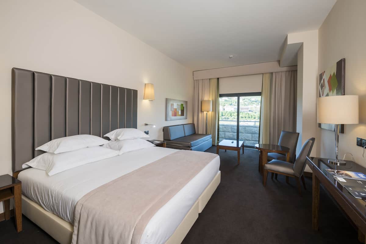 A hotel room with a large bed, a desk, a chair, and a small table.