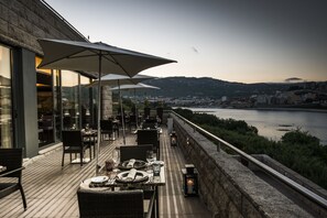 An outdoor dining area with tables and chairs, overlooking a river and cityscape. - Vila Gale Collection Douro Hotel (Lamego)
