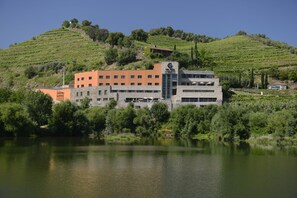 A building with multiple floors, surrounded by lush greenery and a body of water. - Vila Gale Collection Douro Hotel (Lamego)
