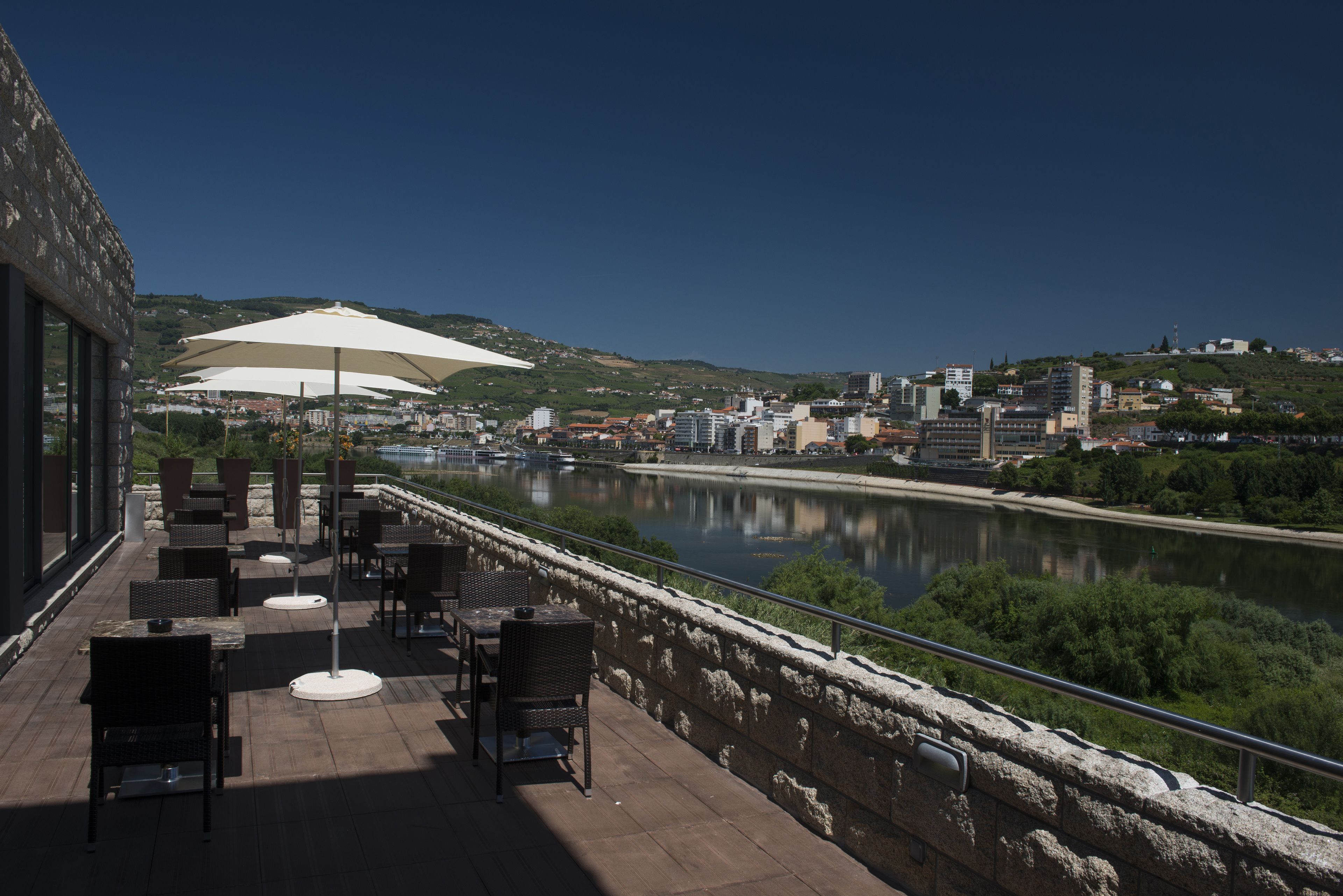 Une terrasse extérieure avec des tables et des chaises, offrant une vue sur une rivière et le paysage urbain.