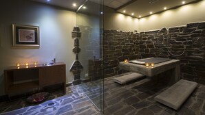 A modern spa room with a stone wall, a glass shower enclosure, and a wooden vanity with candles. - Vila Gale Collection Douro Hotel (Lamego)