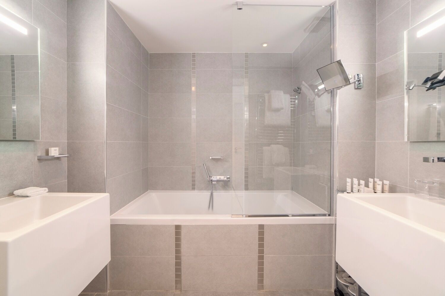 Une salle de bain moderne avec une douche à parois de verre, deux lavabos et une grande baignoire.