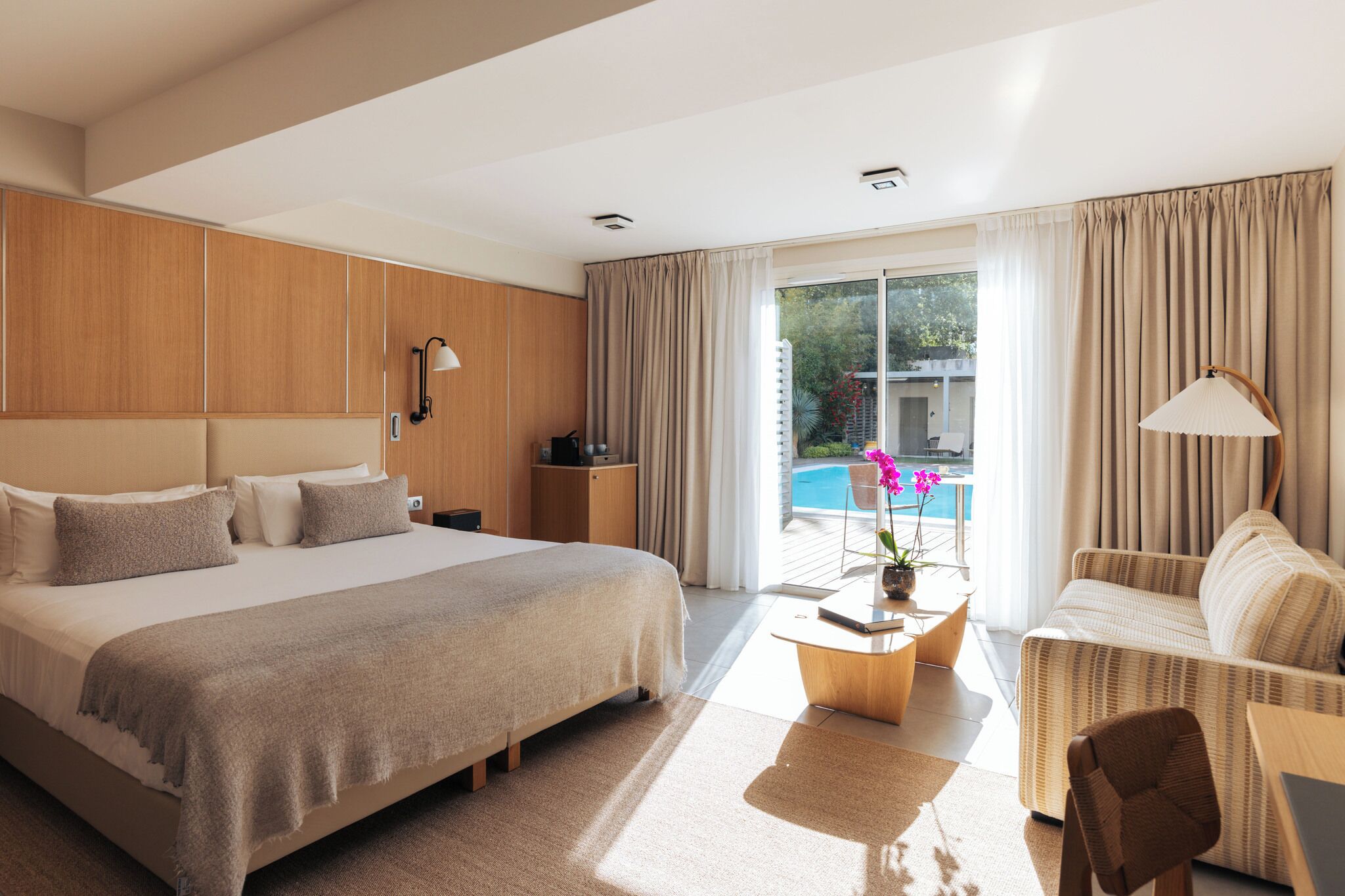 Une chambre d’hôtel moderne dotée d’un grand lit, d’un canapé, d’un bureau et offrant une vue sur une piscine.