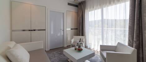 Ett modernt hotellrum med en soffa, ett soffbord, en stol och ett stort fönster med gardiner.