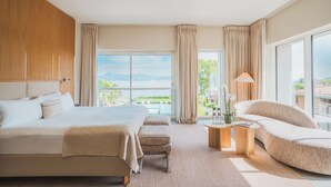 Een hotelkamer met een groot bed, een bank, een klein tafeltje met een lamp, en uitzicht op de zee.