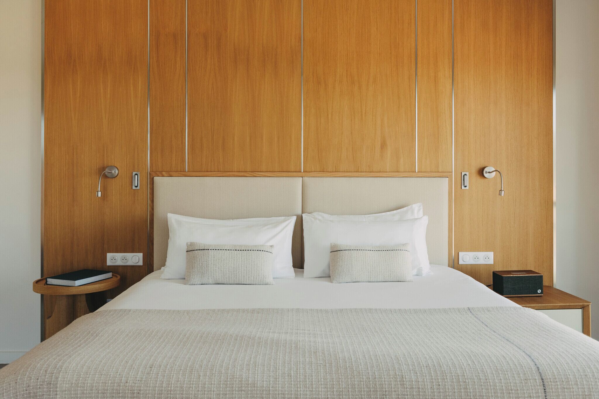Un dormitorio con un armario de madera grande, una cama con ropa de cama blanca, dos mesitas de noche y una lámpara de noche.