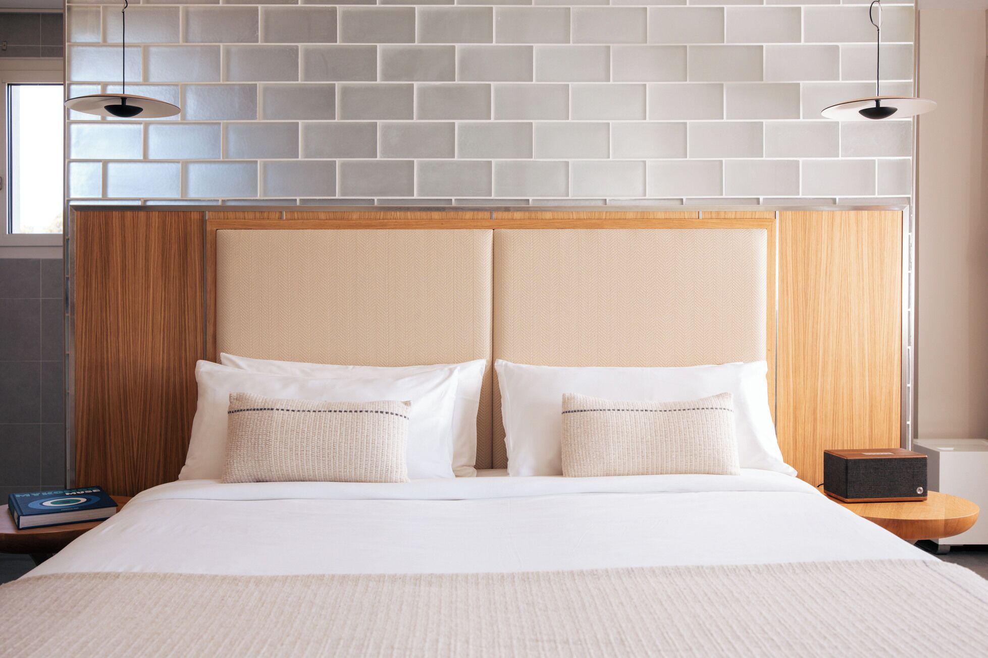 A hotel room with a brick-patterned headboard, two white pillows, a wooden nightstand, and a book.