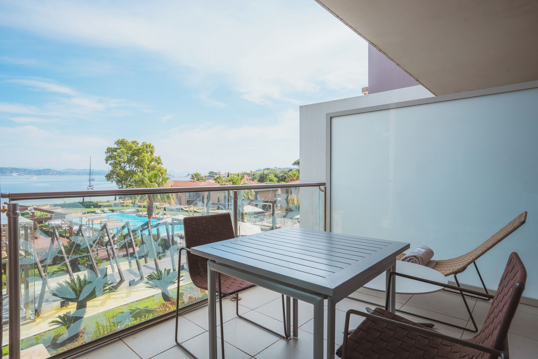A balcony with a table and chairs, overlooking a pool and greenery.