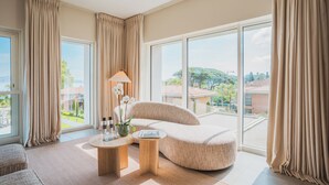 Een moderne woonkamer met een groot raam, een bank, een lamp en een klein tafeltje met decoratieve spullen.