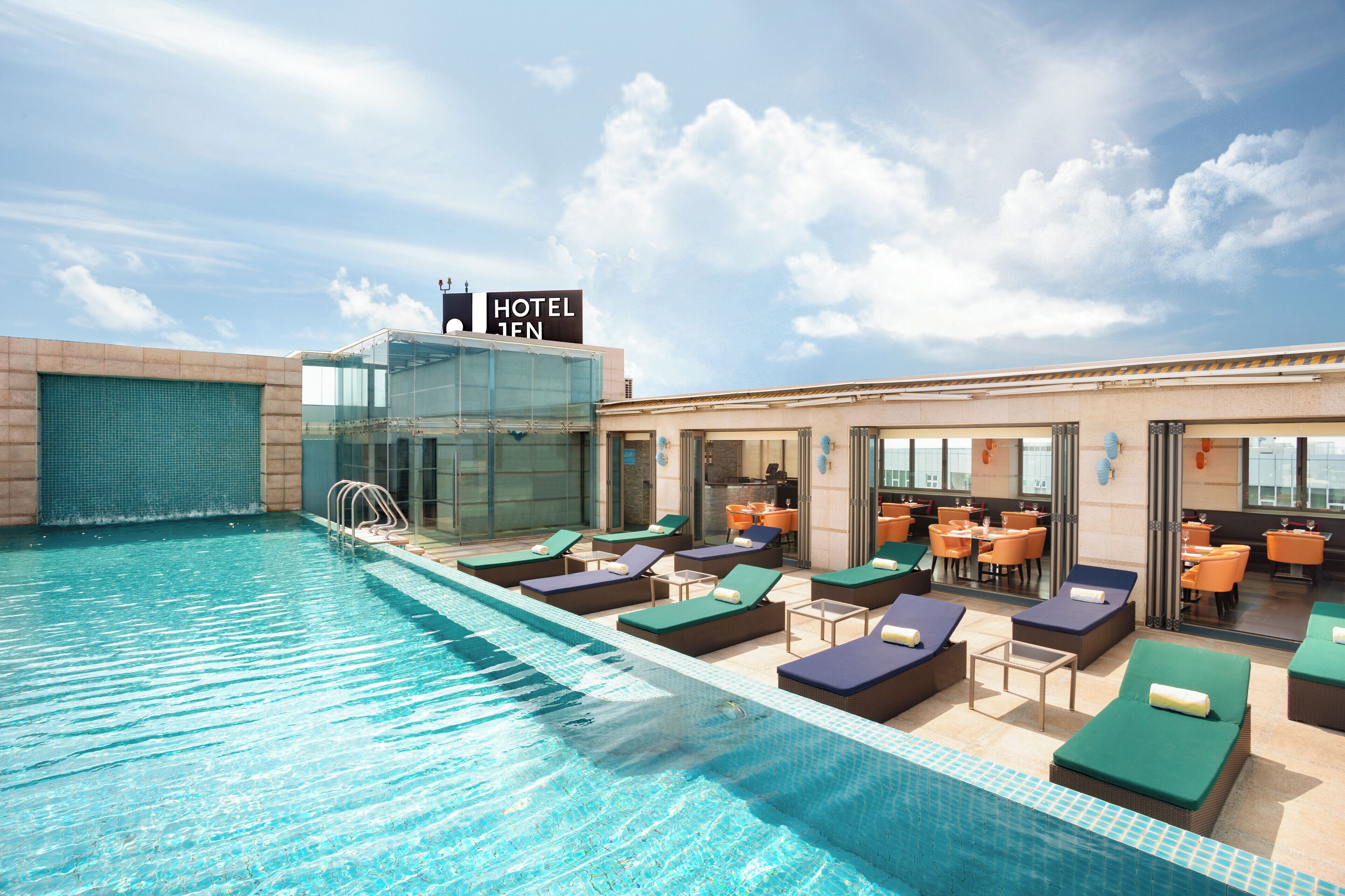 Zona de piscina de hotel con sillones de descanso, una sección con paredes de vidrio y un letrero que dice "HOTEL TEN".