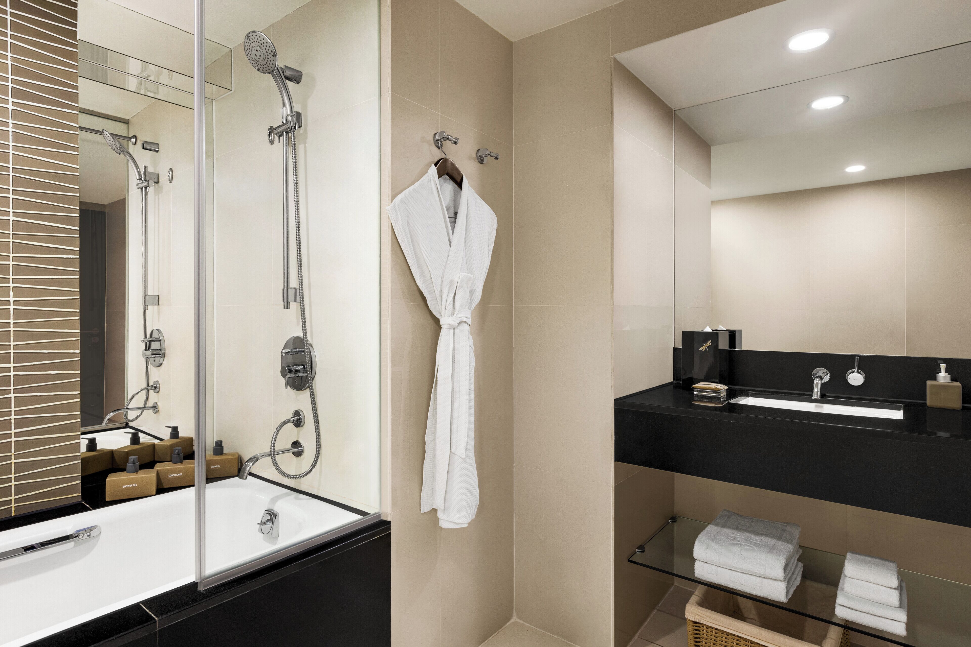 Un baño moderno con bañera, cabina de ducha de vidrio, tocador negro con lavabo y toallas ordenadas.