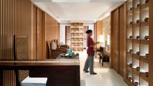 A modern interior with a wooden panel wall, a central seating area with a table, and a shelving unit with pottery. - JEN Maldives Male by Shangri-La (Malé)