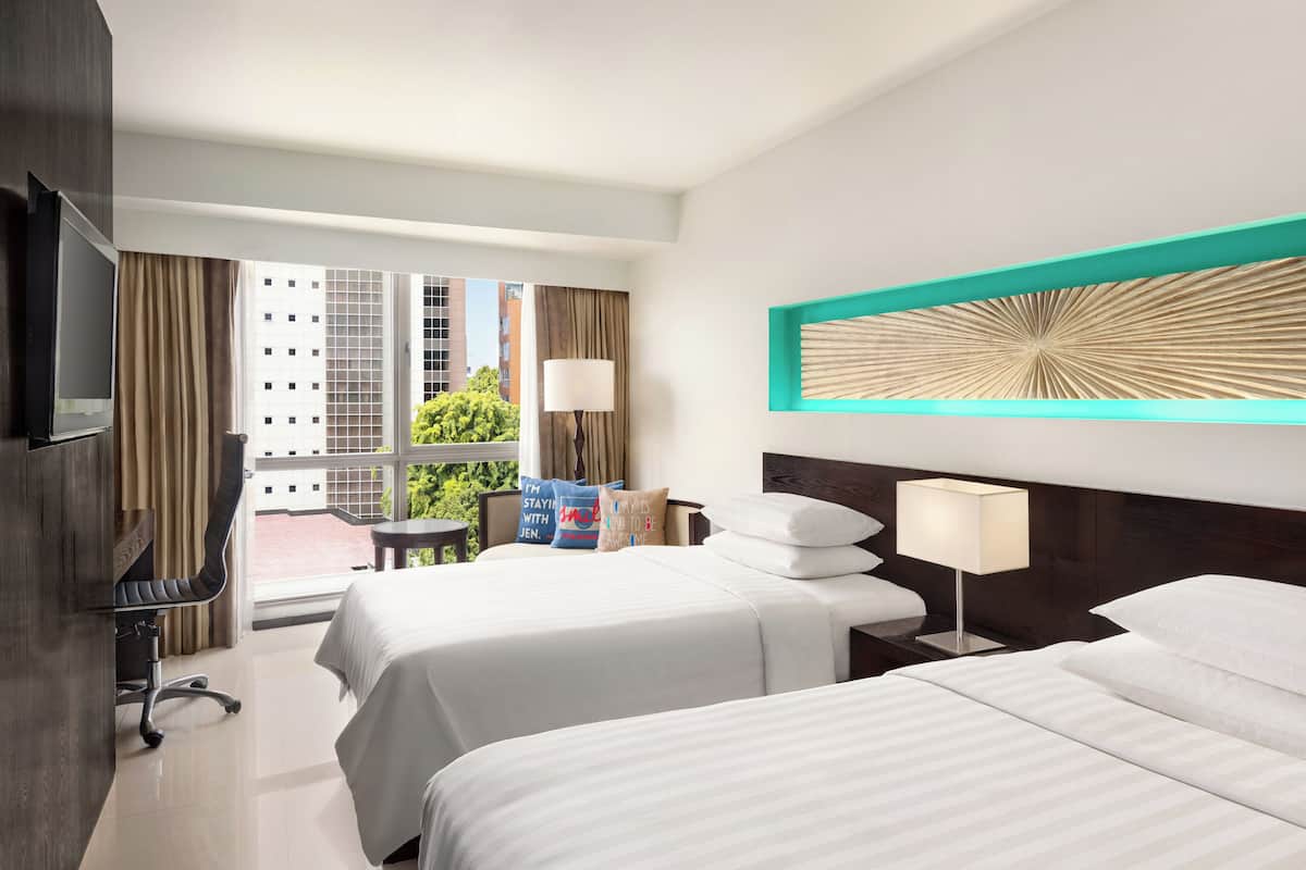 A hotel room with two beds, a desk, a chair, and a TV.
