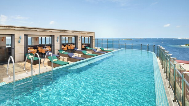 A pool area with lounge chairs and tables, a clear view of the ocean, and a building with large windows. - JEN Maldives Male by Shangri-La (Malé)