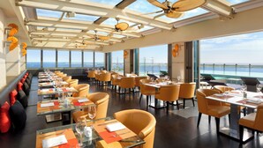 A restaurant with tables and chairs, large windows, and a view of the sea. - JEN Maldives Male by Shangri-La (Malé)