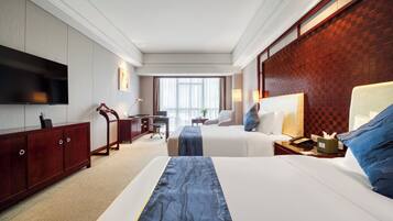 A hotel room with two beds, a desk, a TV, and a view of the outdoors.
