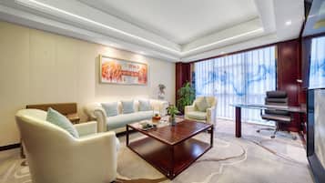 A modern hotel lobby with a sofa, armchairs, a coffee table, a painting, and a large window.