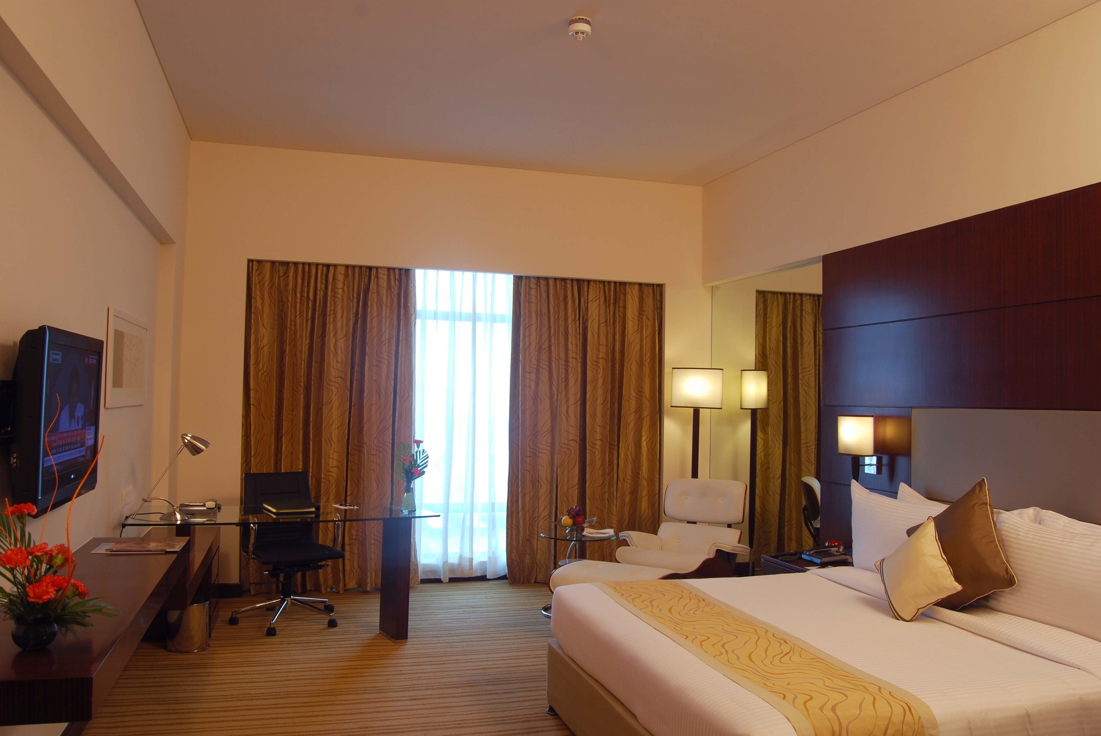 Habitación de hotel con cama, escritorio, silla y televisor.