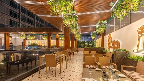 An indoor dining area with wicker furniture, glass tables, and hanging plants. - Country Inn & Suites by Radisson, Sahibabad, Distt Ghaziabad (U.P.) (Ghaziabad)