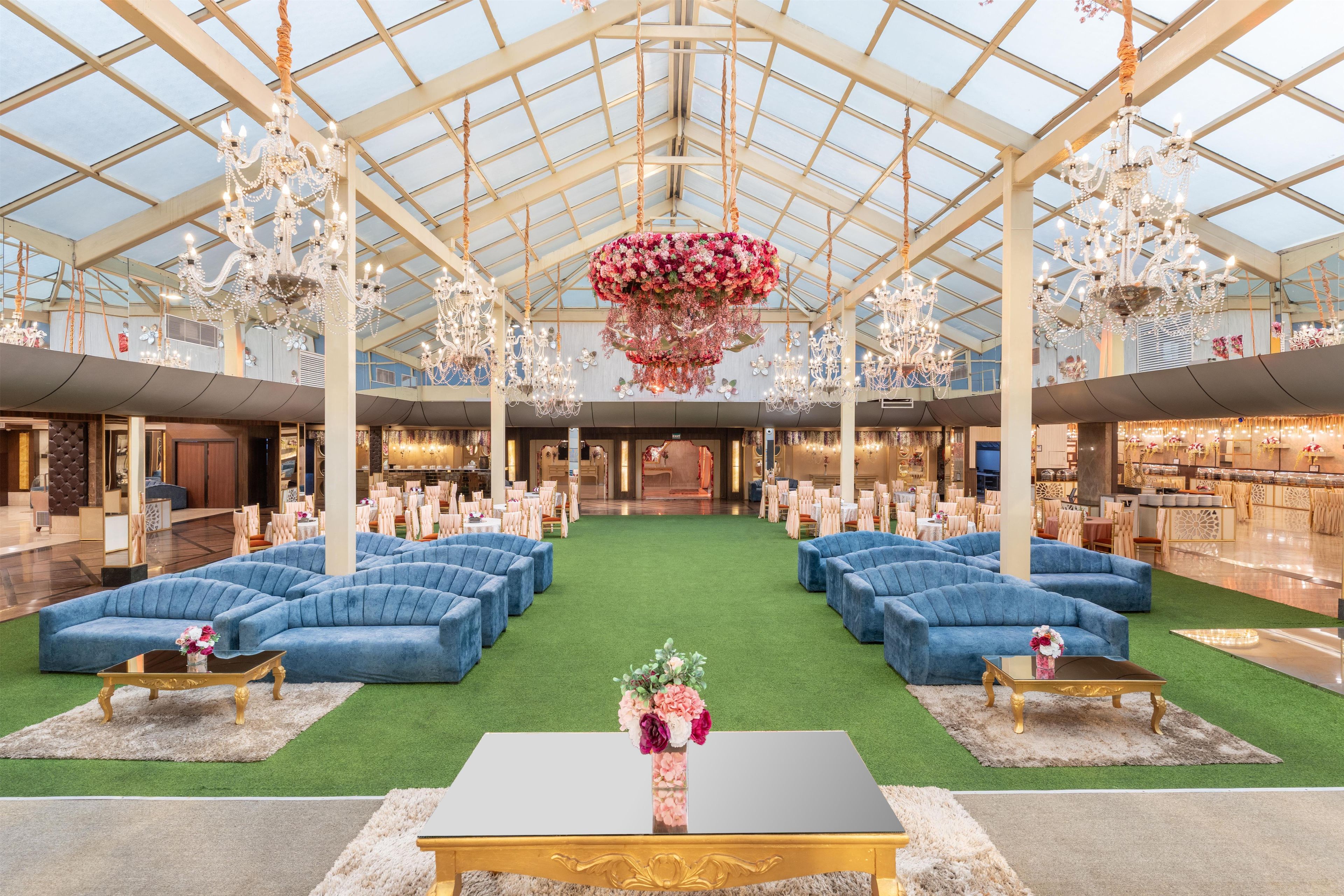 A spacious indoor area with multiple seating arrangements, a central floral arrangement, and a high ceiling with natural light.