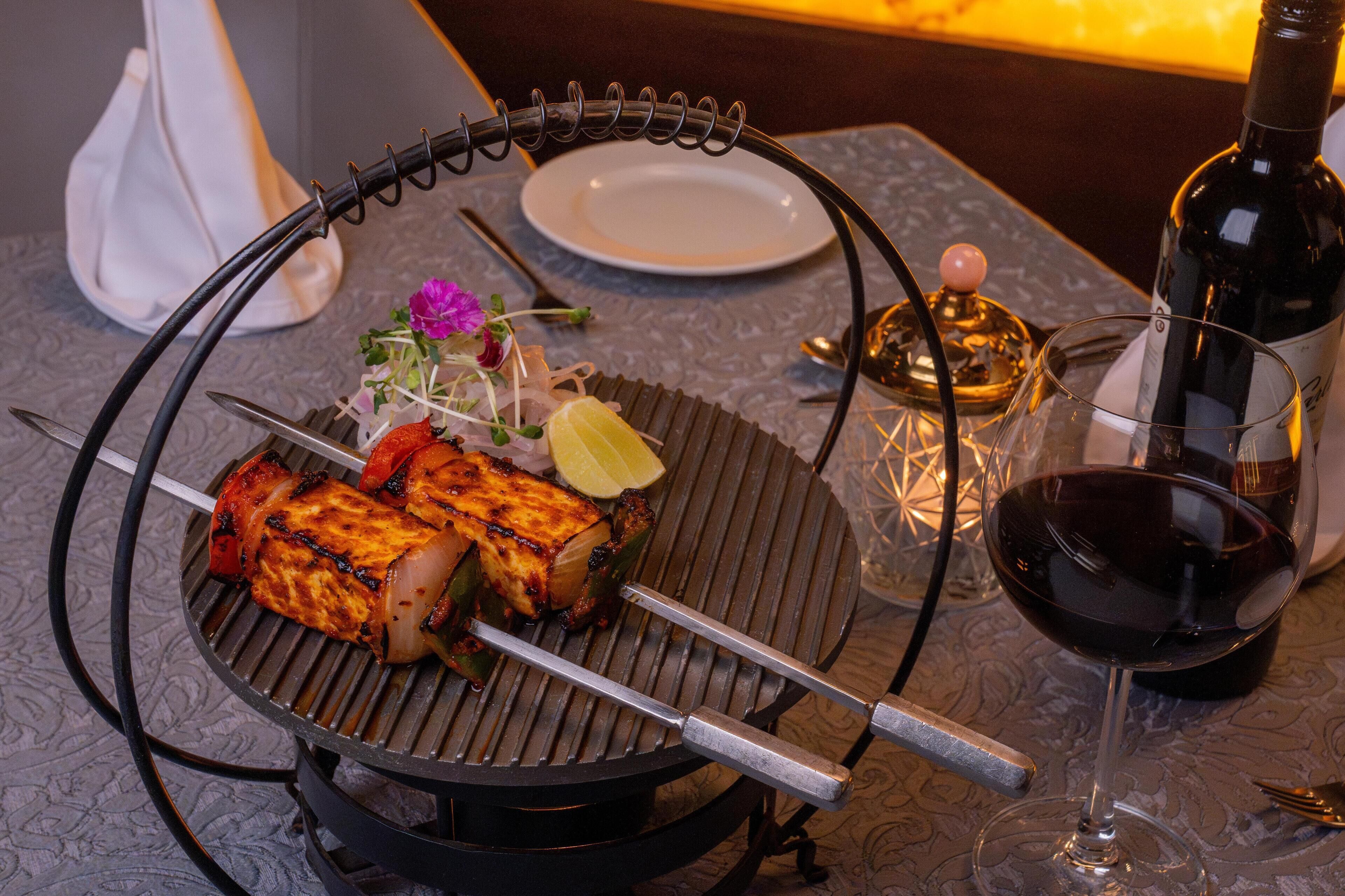 A table with a grill, a bottle of wine, a glass of wine, a plate, and a small vase with flowers.