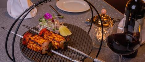 A table with a grill, a bottle of wine, a glass of wine, a plate, and a small vase with flowers.