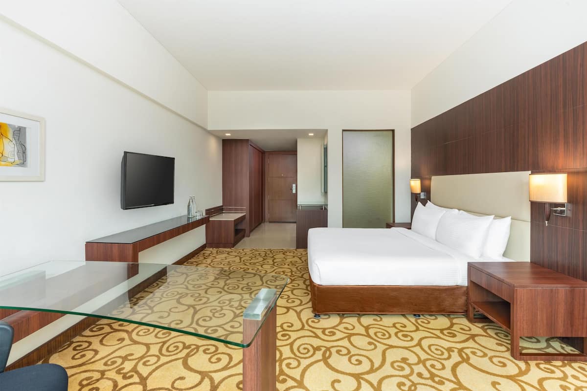 A hotel room with a bed, a TV, a desk, and a glass coffee table.