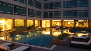 A large indoor swimming pool with multiple lounge areas and a modern building with large windows in the background. - Country Inn & Suites by Radisson, Sahibabad, Distt Ghaziabad (U.P.) (Ghaziabad)