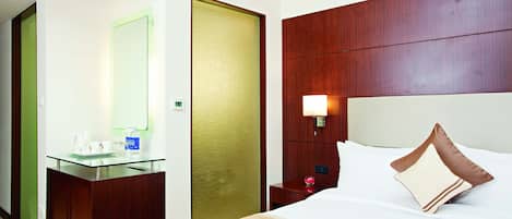 A hotel room with a wooden headboard, a glass bedside table, a bed with white bedding, and a nightstand with a lamp.