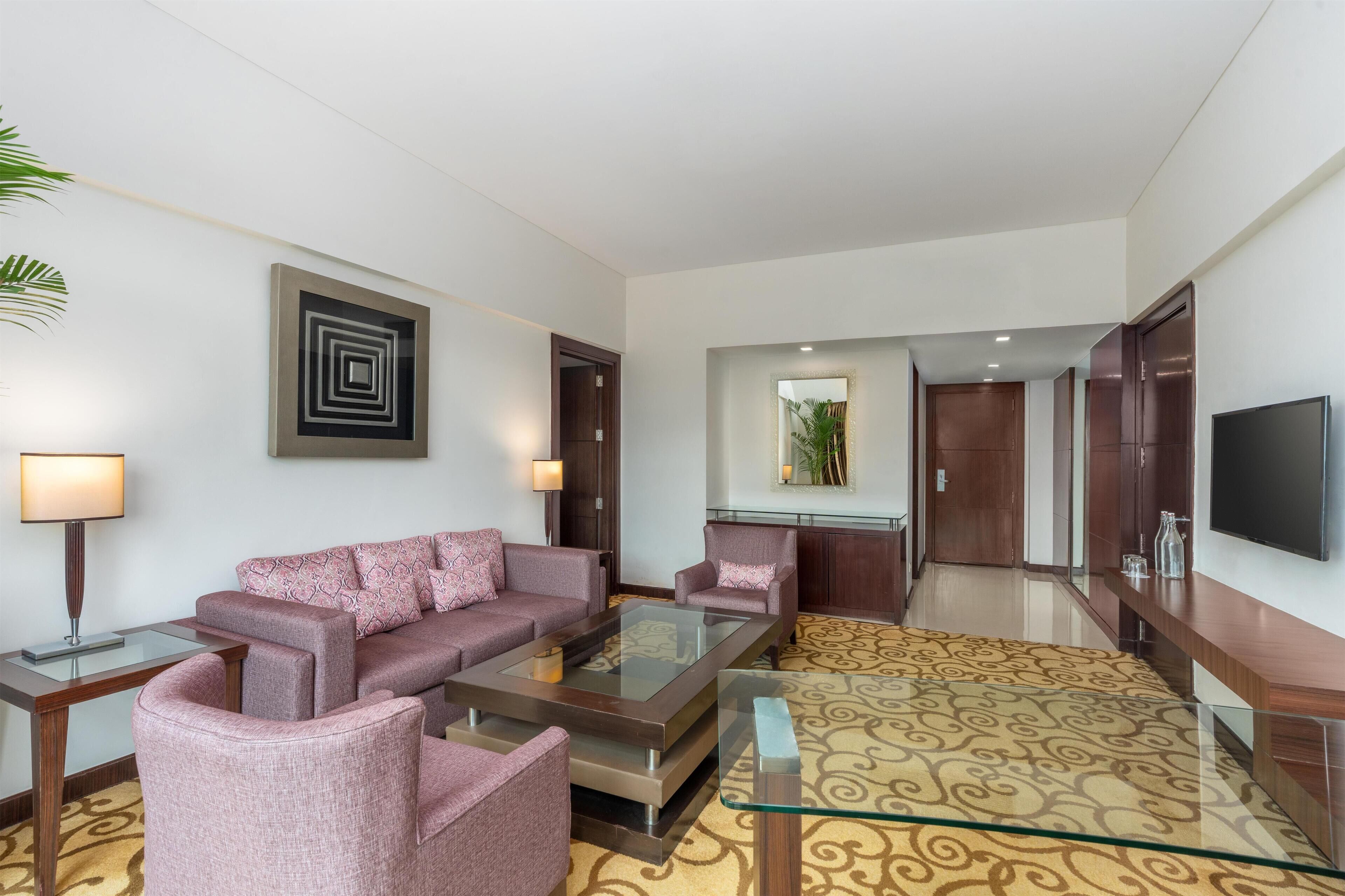 Un hall d’hôtel moderne avec un ensemble de canapés, une table basse, un téléviseur et une moquette à motifs.