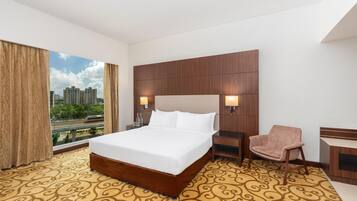 Habitación de hotel con una cama grande, una silla, un escritorio y vistas a la ciudad.