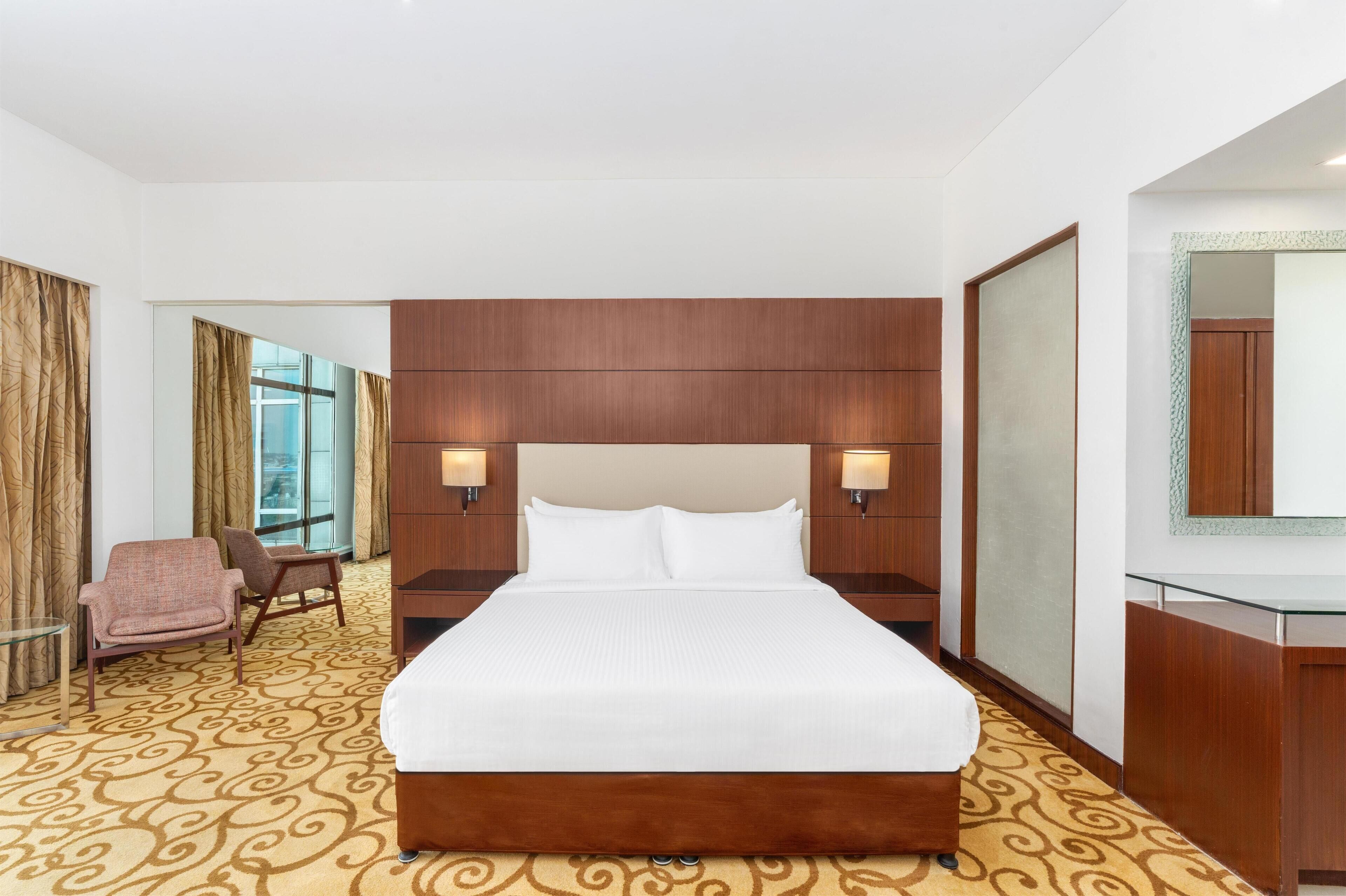 Une chambre d’hôtel avec un grand lit, deux tables de chevet, une chaise, un bureau et un miroir.