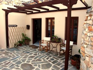 Un patio con suelo de piedra, una zona de recepción, sillas de madera y plantas en macetas.