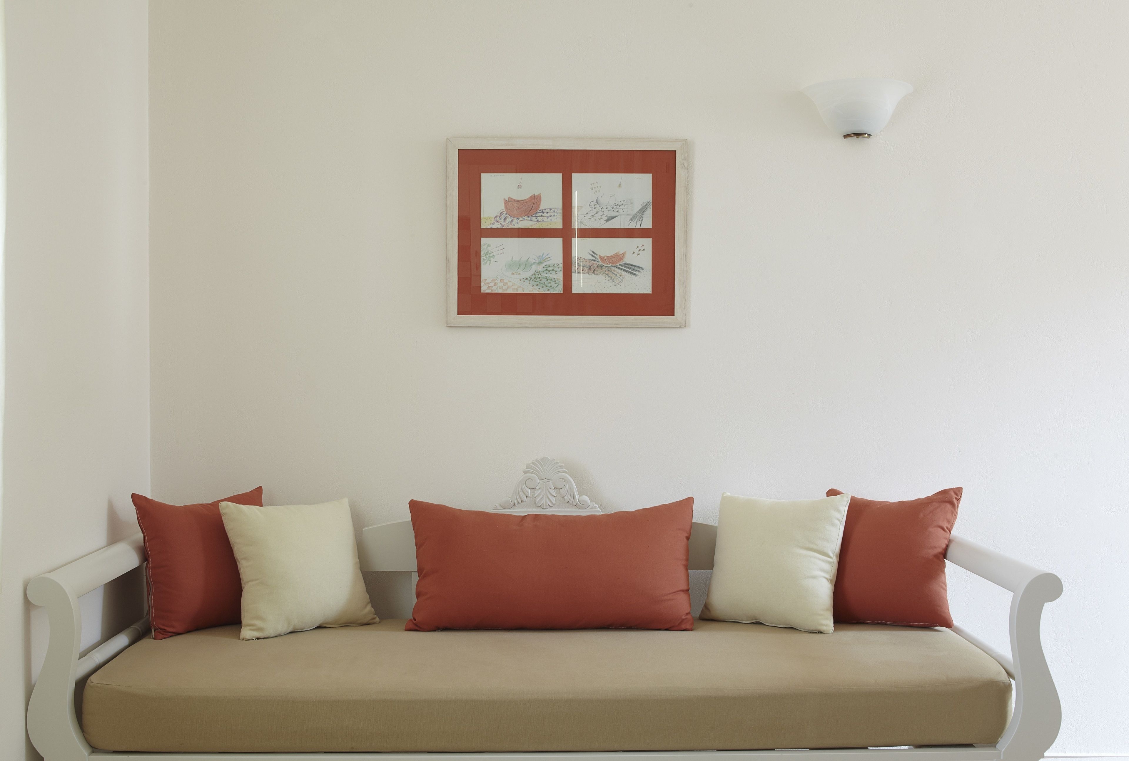 A white sofa with a beige cushion and four pillows in red and white.