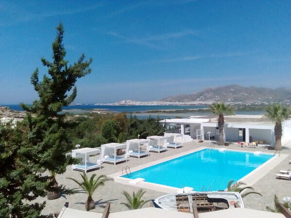 Zona de piscina con sillones de descanso, un barco y vistas al mar y al paisaje urbano.