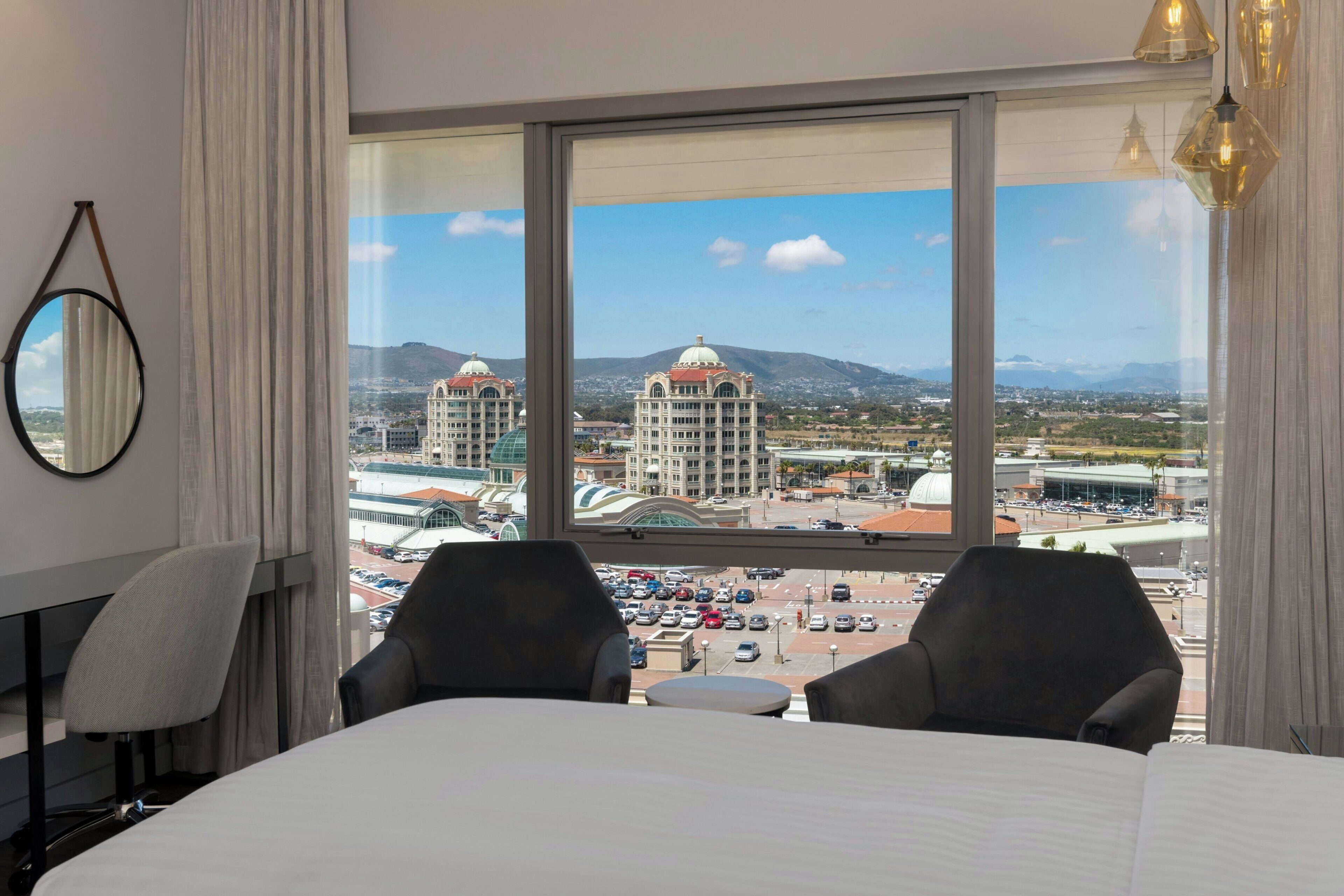 Ein Hotelzimmer mit großem Fenster und Blick auf die Stadt, einschließlich Gebäude und Berge.