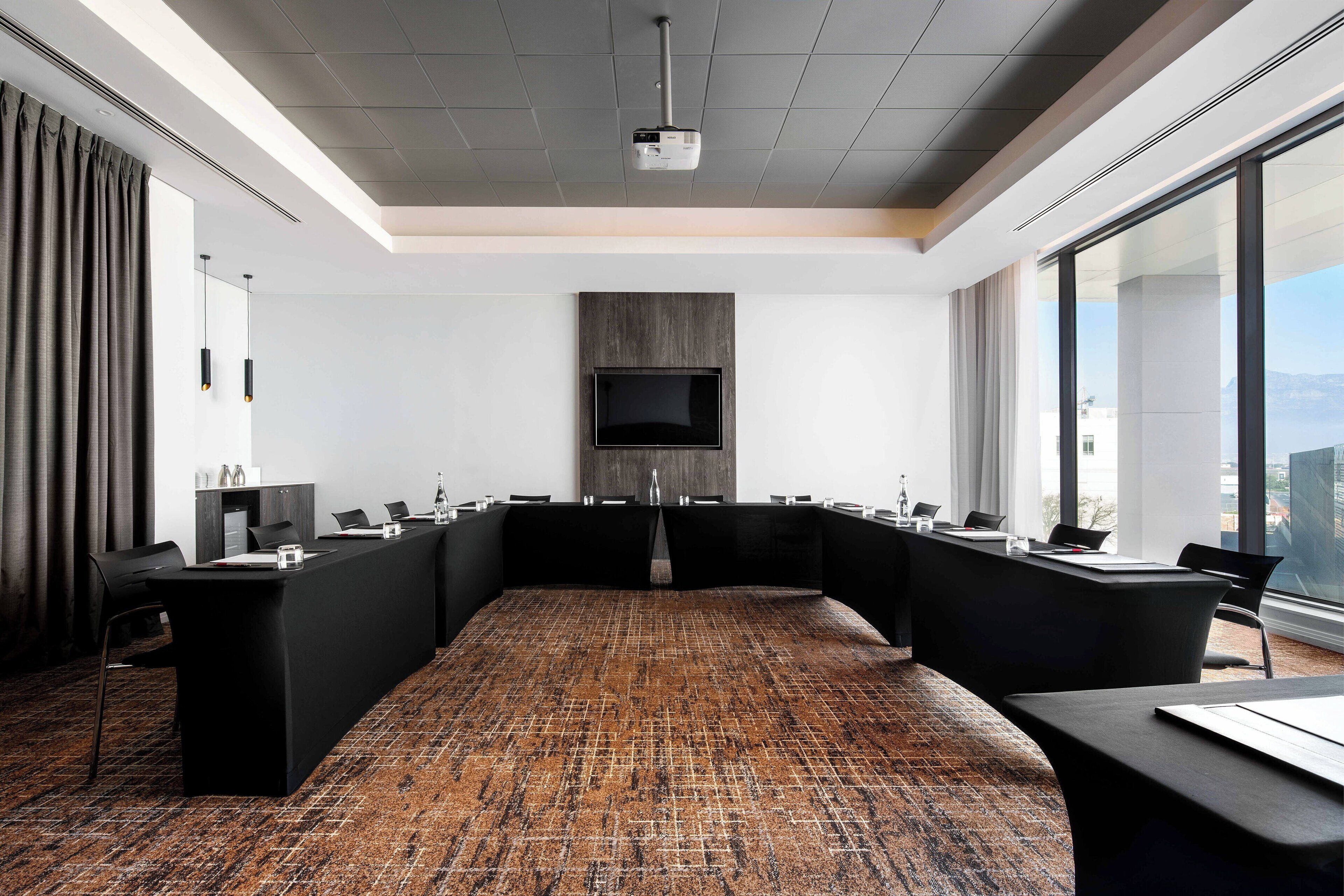 A conference room with a long table, multiple chairs, a flat-screen TV, and a projector.