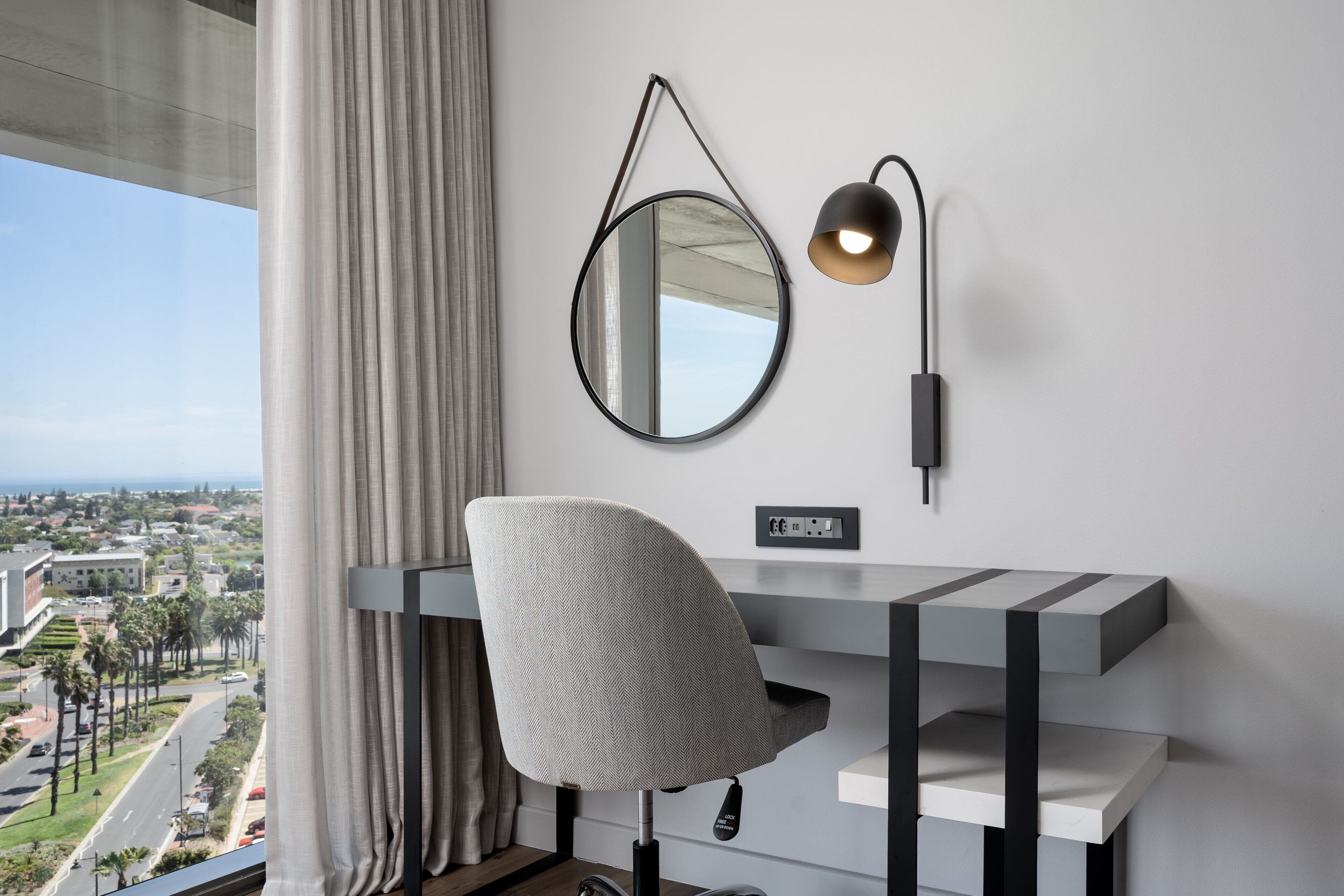 A modern desk with a chair, a wall-mounted mirror, and a lamp.