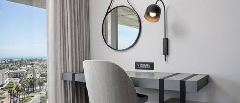 A modern desk with a chair, a wall-mounted mirror, and a lamp.