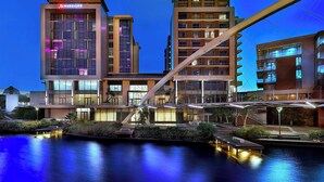 Un hôtel moderne arborant le logo Marriott, doté d’une piscine sur le toit et d’un pont reliant les différentes parties de l’établissement.