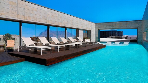 Une piscine à débordement située sur le toit, avec des chaises longues, une terrasse en bois et une vue dégagée sur les montagnes.