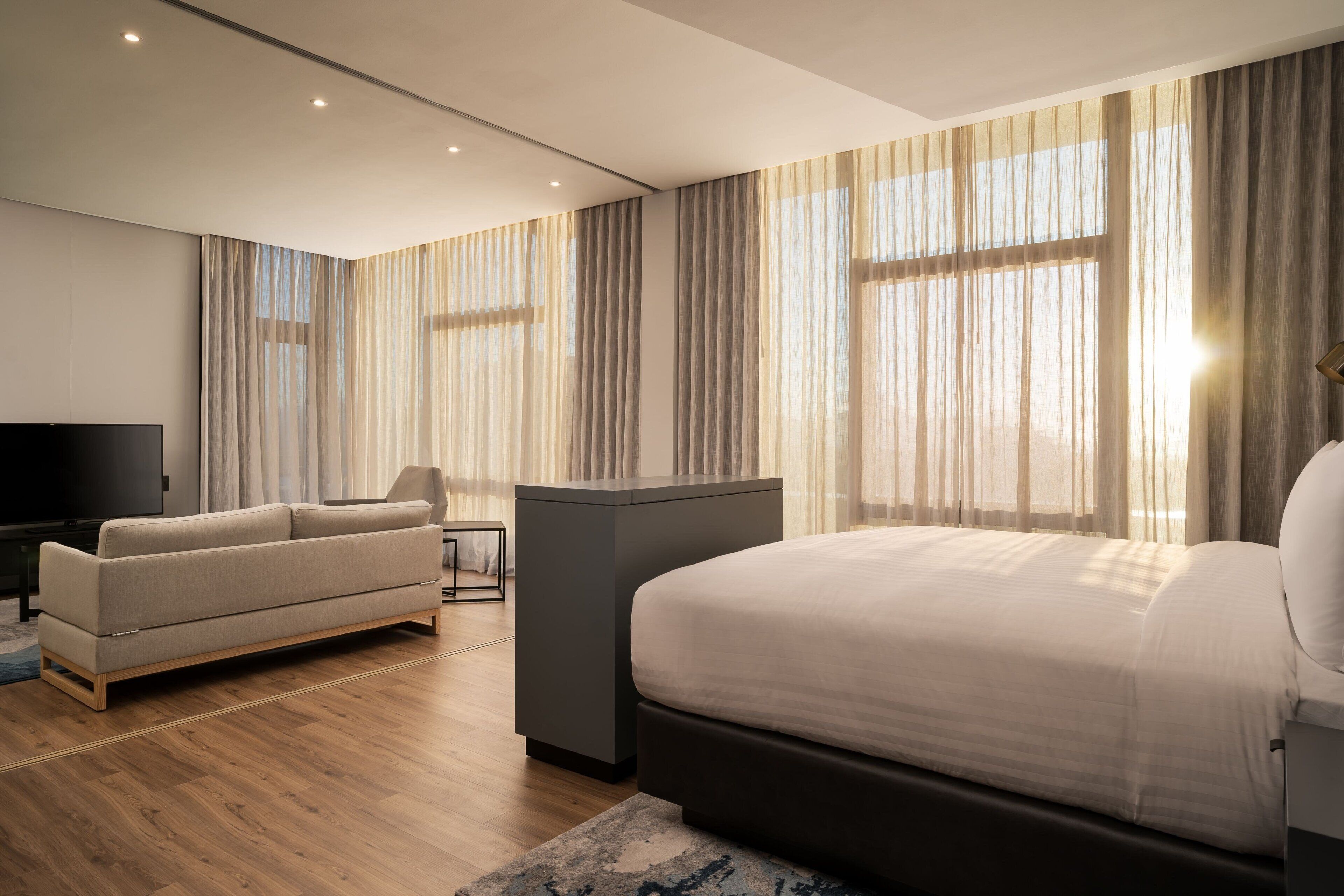 A modern hotel room with a large bed, a sofa, a TV, and a desk.