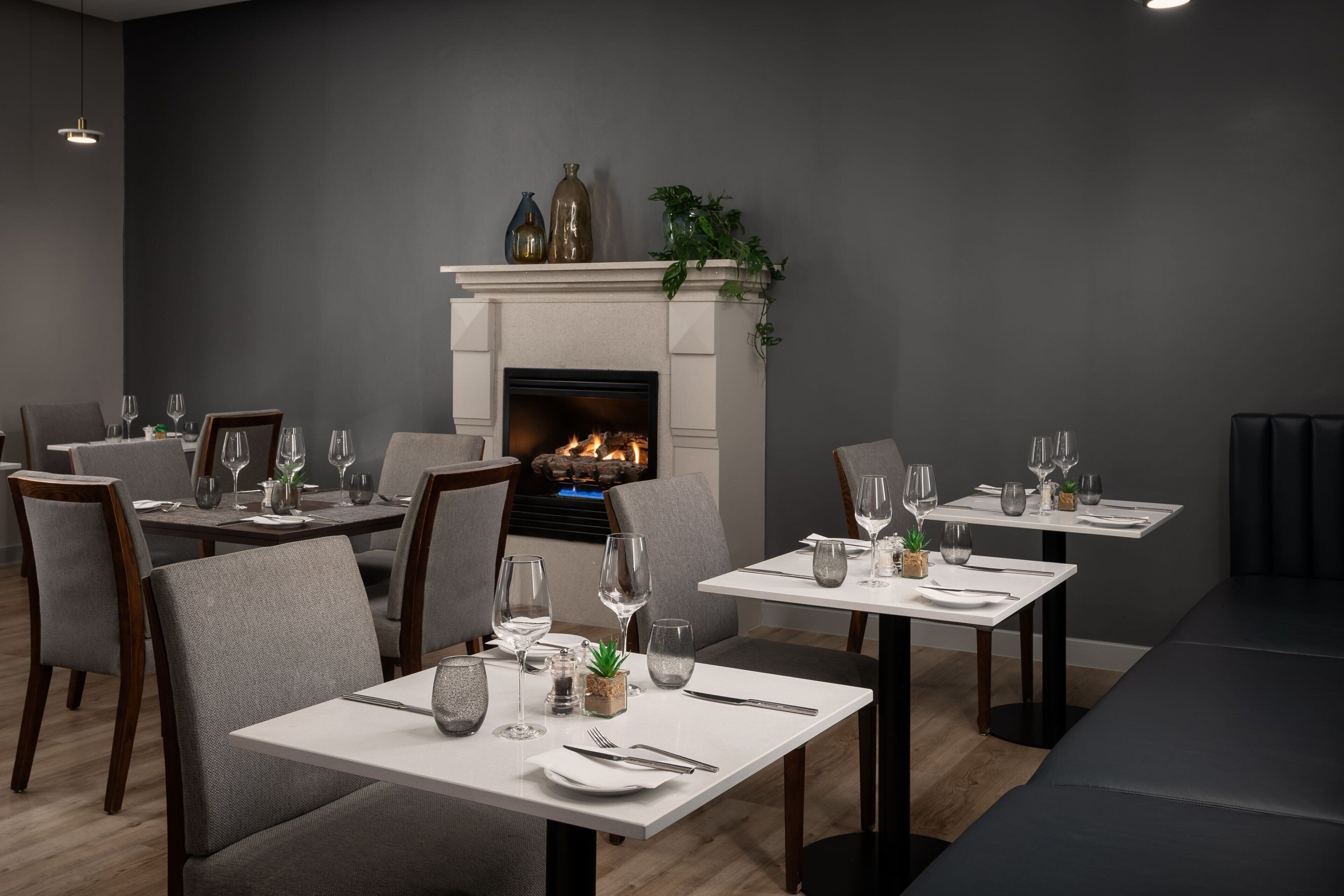 A modern dining area with tables set for two, a fireplace, and a minimalist decor.