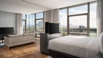 Ein modernes Hotelzimmer mit einem großen Bett, einer Couch, einem Flachbildfernseher und großen Fenstern mit Blick auf die Stadt.