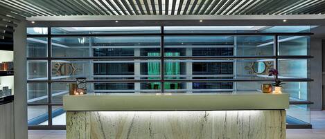 Un área de recepción moderna con mostrador de mármol, amplias ventanas de vidrio y un techo con vigas horizontales.