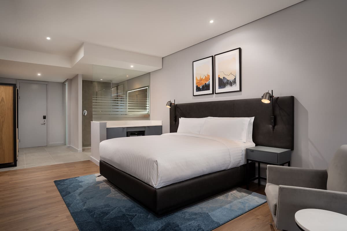 A modern bedroom with a large bed, bedside tables, a chair, and a desk with a mirror.