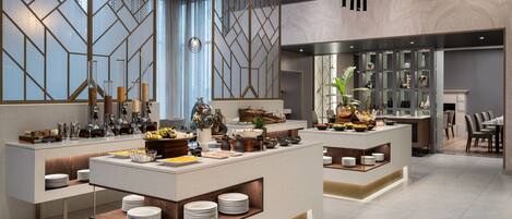 Un moderno vestíbulo de hotel con una zona de buffet central, arreglos de asientos y una pared decorativa con patrones geométricos.