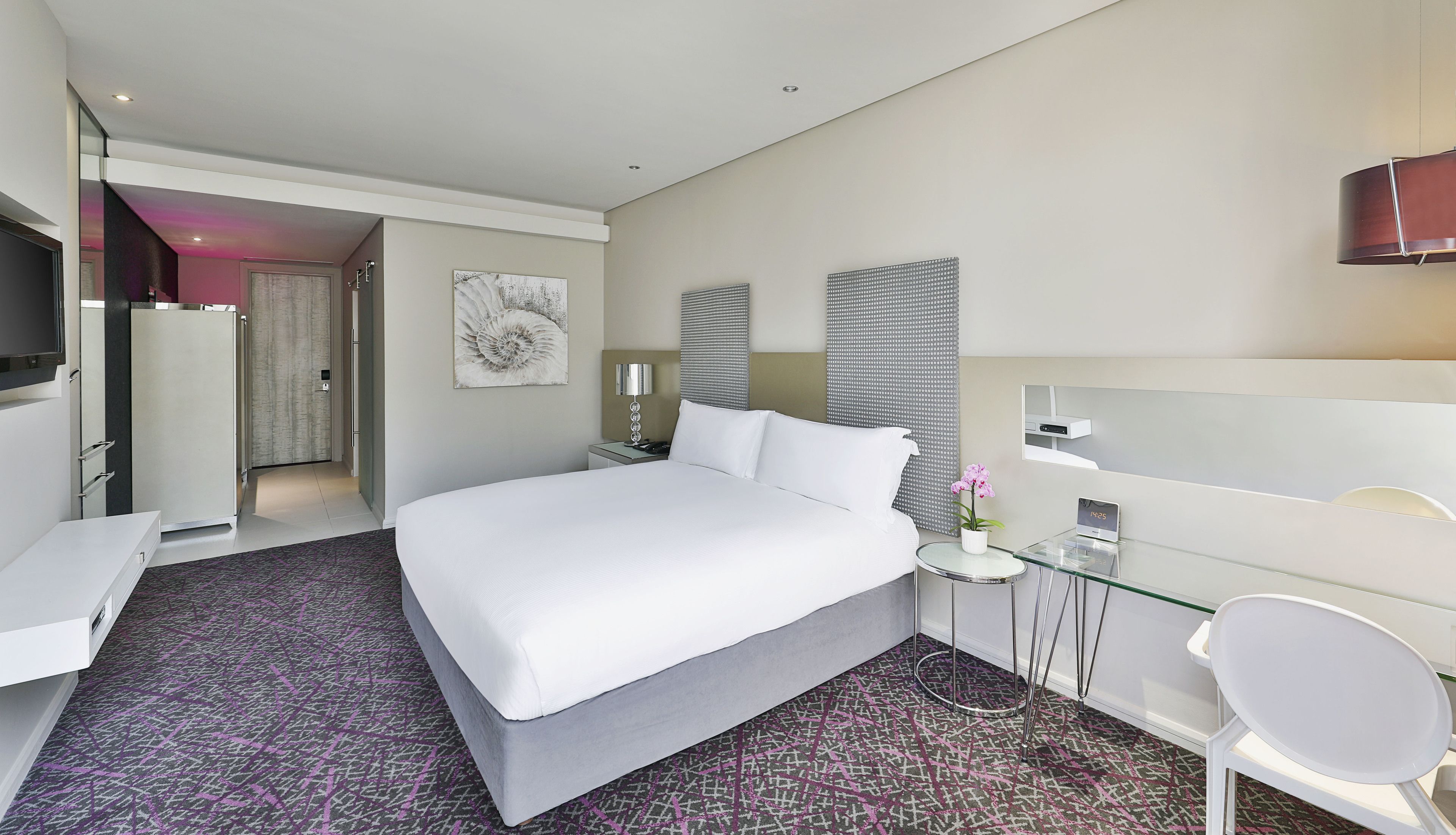 A modern hotel room with a large bed, a desk, a chair, and a TV.